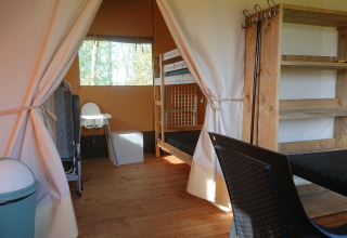 Binnenzicht van een glamping safaritent met stapelbed, houten rek, tafel en stoelen op camping Drenthe.