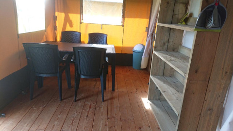 Interior view of a glamping safari tent with dining table, four plastic chairs, shelving, and wood floor.