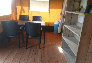 Vue intérieure d’une tente safari glamping avec table à manger, quatre chaises en plastique et étagères.