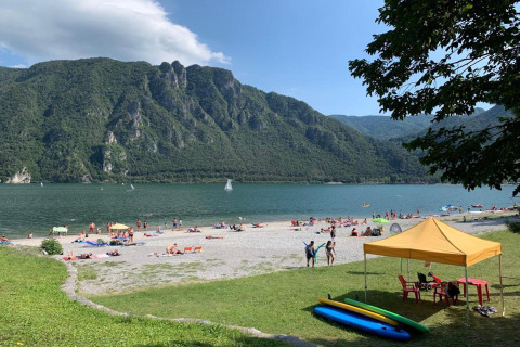 Beach scene at Lago Idro with mountains, sunbathers, tents, and paddleboards in Lombardy, Italy.