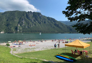 Scène de plage au Lago Idro avec montagnes, baigneurs, tentes et paddleboards en Lombardie, Italie.