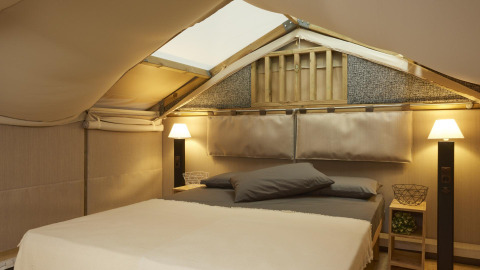 Vista interior de tienda glamping de lujo en Lago Idro Glamping Boutique Lombardía con cama doble y lámparas.