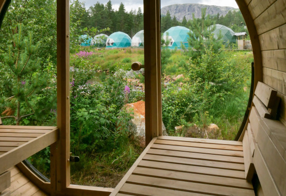 Uitzicht vanuit een houten sauna naar de groene natuur en glampingkoepels bij Brokkestøylen in Agder.