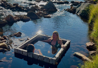 Twee mensen ontspannen in een houten vierkante bak in een rivier bij Brokkestøylen - Domes in Agder.