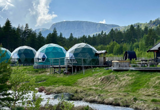 Geodætiske kupler til glamping ved Brokkestøylen i Agder, omgivet af skov, bæk og bjerge i baggrunden.