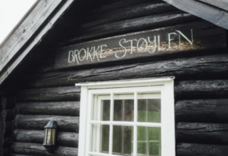 Cabina in legno con insegna 'Brokke Støylen' sopra la finestra, glamping o campeggio in Agder.