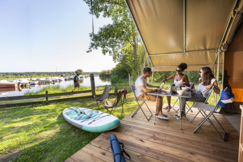 Drei Personen frühstücken auf der Terrasse am Wasser im Huttopia Lac d’Aureilhan Glamping, Mimizan.