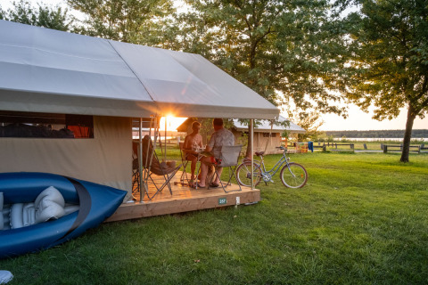 Pareja disfruta la puesta de sol fuera de su tienda glamping en Huttopia Lac d’Aureilhan – Mimizan, Nouvelle-Aquitaine.