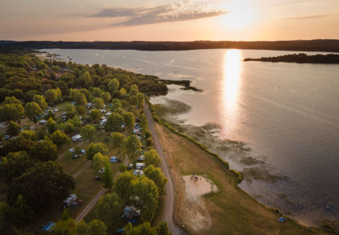 Luftaufnahme von Huttopia Lac d’Aureilhan – Mimizan Glampingplatz am Seeufer bei Sonnenuntergang.