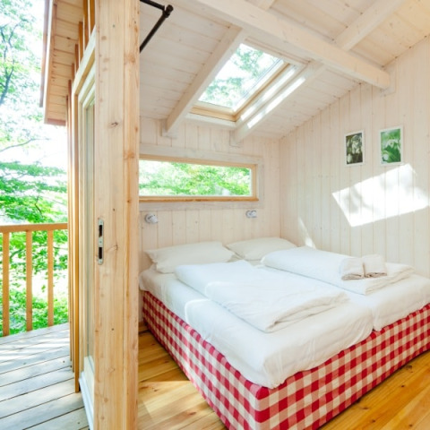 Camera glamping luminosa presso Wipfelglück Baumhaushotel con letto matrimoniale, lucernari e vista bosco.