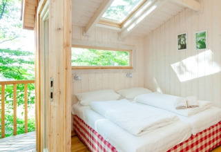 Bright glamping bedroom at Wipfelglück Baumhaushotel with large skylights, double bed, and forest views.