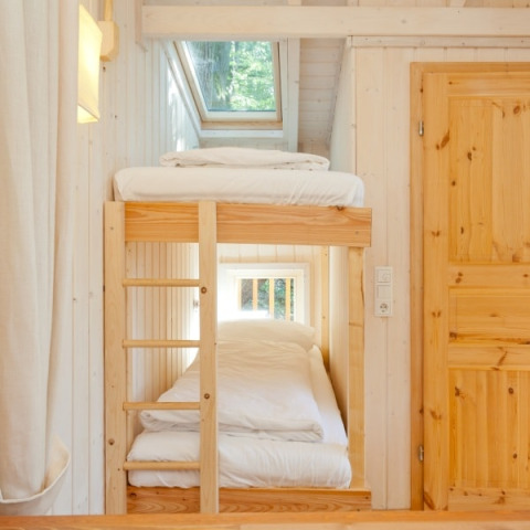 Lits superposés douillets au Wipfelglück Baumhaushotel avec intérieur en bois et grandes fenêtres.