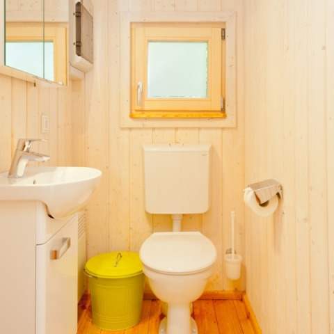 Helles Badezimmer mit Holzwänden, weißer Toilette, Waschbecken und grünem Mülleimer im Wipfelglück Baumhaushotel.