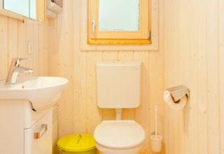 Bright bathroom with wooden walls, white toilet, washbasin, and green trash bin at Wipfelglück Baumhaushotel.