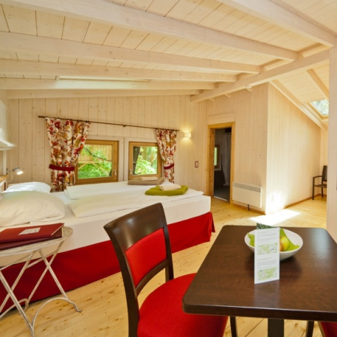 Interieur van Wipfelglück Baumhaushotel boomhut met houten vloer, tweepersoonsbed en eettafel in de kamer.