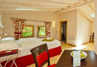 Indvendig udsigt af Wipfelglück Baumhaushotel glamping værelse med trægulve, dobbeltseng og spisebord.