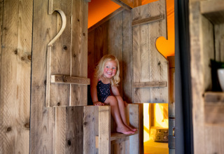 Fillette souriante assise dans une tente en bois à Villa la Diva - Safaritenten Le Marche, glamping Italie.