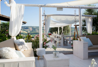 Área de lounge y comedor al aire libre con toldos y vista a las colinas en Villa la Diva Le Marche glamping.