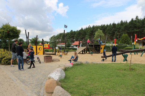 Familias y niños juegan en el parque infantil de Campingpark Buntspecht - Pods Brandenburg, rodeado de naturaleza.
