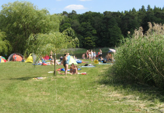 Campingpark Buntspecht - Pods Brandenburg: famiglie, tende e bambini che giocano vicino a un lago erboso.