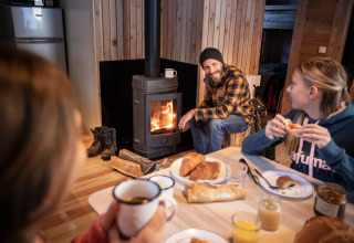 Familie frühstückt gemütlich in Holzhütte mit Kamin bei Huttopia Vanoise – Champagny Winter in den Alpen.