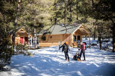 Familie genießt Schneeschuhwandern vor Holzhütten bei Huttopia Vanoise – Champagny Glamping in Auvergne-Rhône-Alpes.