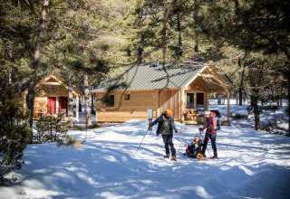 Familia disfrutando en la nieve frente a cabañas de madera en Huttopia Vanoise – Champagny glamping en Auvergne-Rhône-Alpes.