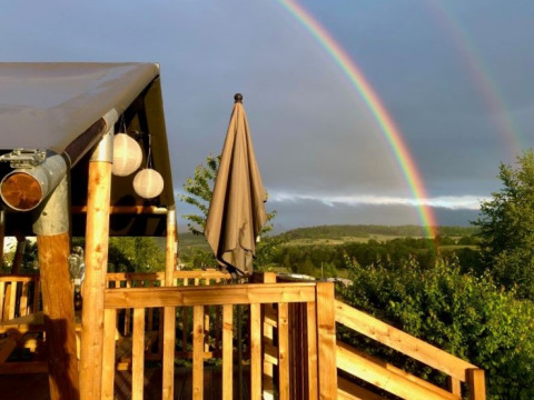 Glamping en Camping Groß-Eichen en Hessen, terraza de madera y doble arco iris visible al fondo.