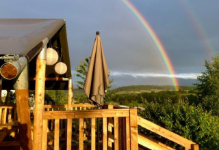 Glamping bij Camping Groß-Eichen in Hessen met houten terras en een dubbele regenboog op de achtergrond.