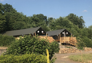 To luksustelte på Camping Groß-Eichen i Hessen, omgivet af grønne træer og natur under klar blå himmel.
