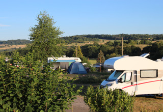 Campingplads med autocampere, telte og grøn udsigt på Camping Groß-Eichen - Safaritenten Hessen i solskin.