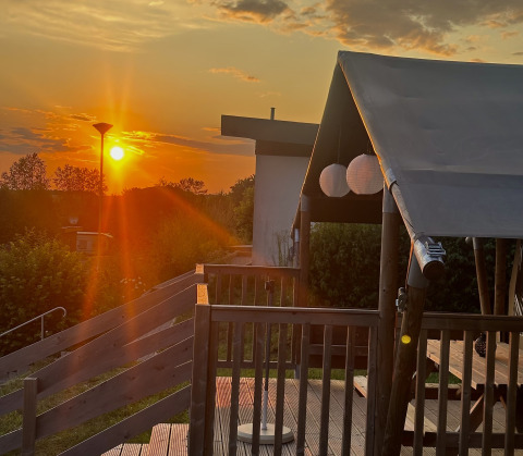 Zonsondergang bij glampingaccommodatie met houten terras, Camping Groß-Eichen - Safaritenten Hessen.