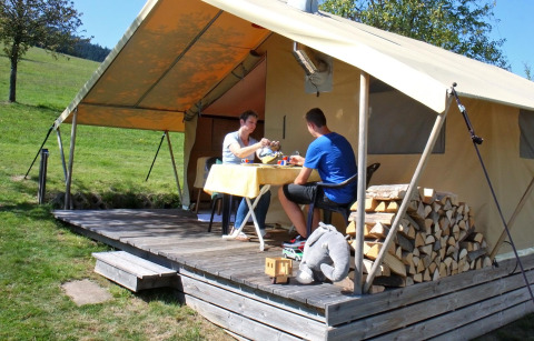 Two people enjoy a meal outside a glamping tent with firewood at Camping Schwarzwaldhorn in Baden-Württemberg.