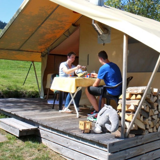 Deux personnes prennent un repas devant une tente glamping avec bois au Camping Schwarzwaldhorn, Baden-Württemberg.