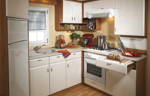 Cocina moderna de camping en glamping con gabinetes blancos y estufa de gas, nevera y verduras frescas.