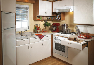 Cucina moderna da campeggio in glamping con mobili bianchi, fornello a gas, frigorifero e verdure fresche.