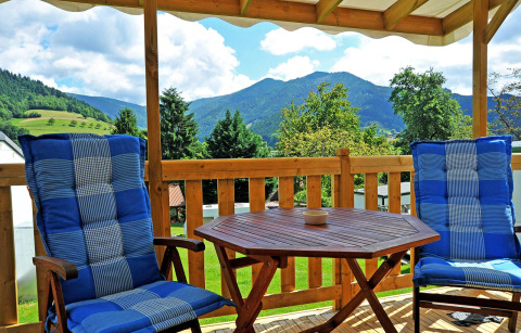 Cozy terrace with blue cushioned chairs, wooden table, mountain views at Camping Schwarzwaldhorn glamping site.