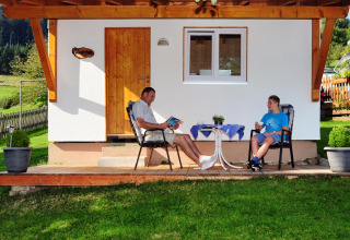 Dos personas se relajan fuera de una cabaña glamping en Camping Schwarzwaldhorn, Baden-Württemberg, disfrutando el entorno.