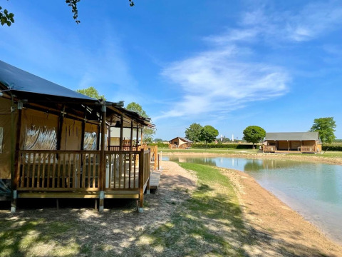 Glamping-indkvartering ved en sø hos De Betuwse Hofjes - Betuwe Lodges i Gelderland, Holland, under blå himmel.