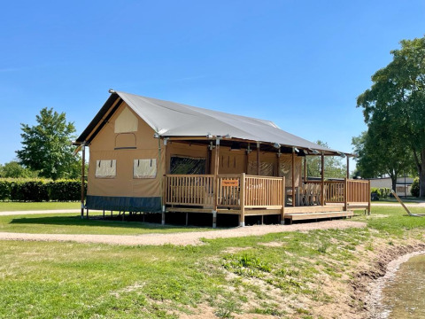 Hébergement glamping au bord du lac chez De Betuwse Hofjes - Betuwe Lodges Gelderland sous un ciel bleu clair.