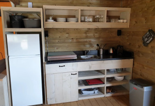 Keukenhoek in een glamping lodge bij De Betuwse Hofjes in Gelderland met houten planken en koelkast.