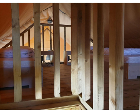 Vista interna di una tenda glamping con pavimento in legno, due letti singoli e divisori in legno.