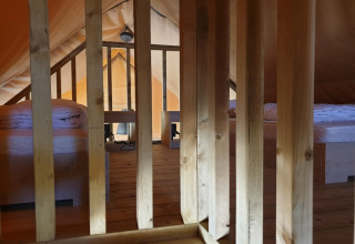 Vue intérieure d'une tente glamping avec sol en bois, deux lits simples et des barreaux en bois séparateurs.