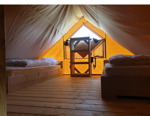 Binnenkant van een glamping-tent met houten vloer, twee bedden en een kast bij De Betuwse Hofjes, Gelderland.