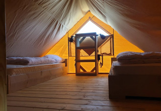 Innenansicht eines Glamping-Zelts mit Holzboden, zwei Betten und Regal bei De Betuwse Hofjes in Gelderland.