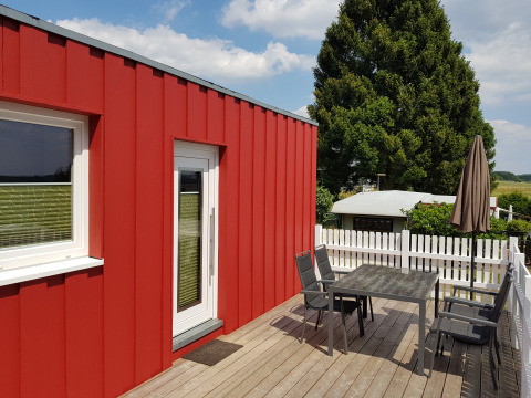 Alloggio glamping rosso con terrazza, tavolo, sedie e ombrellone a Camping im Bergischen Land, Renania Settentrionale-Vestfalia.