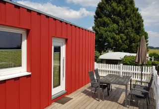 Red glamping accommodation with terrace, table, chairs and umbrella at Camping im Bergischen Land, North Rhine-Westphalia.