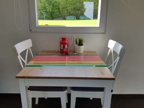Gezellig eetplekje met twee witte stoelen, gestreepte placemat en uitzicht op het grasveld buiten.