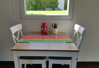 Cozy dining nook for two with white chairs, a striped placemat, and view of a green field through window.