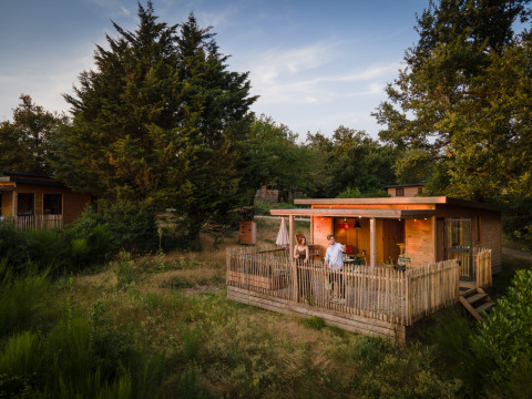 Glamping accommodatie bij Village Huttopia Pays de Condrieu: houten cabin met terras in groene omgeving.